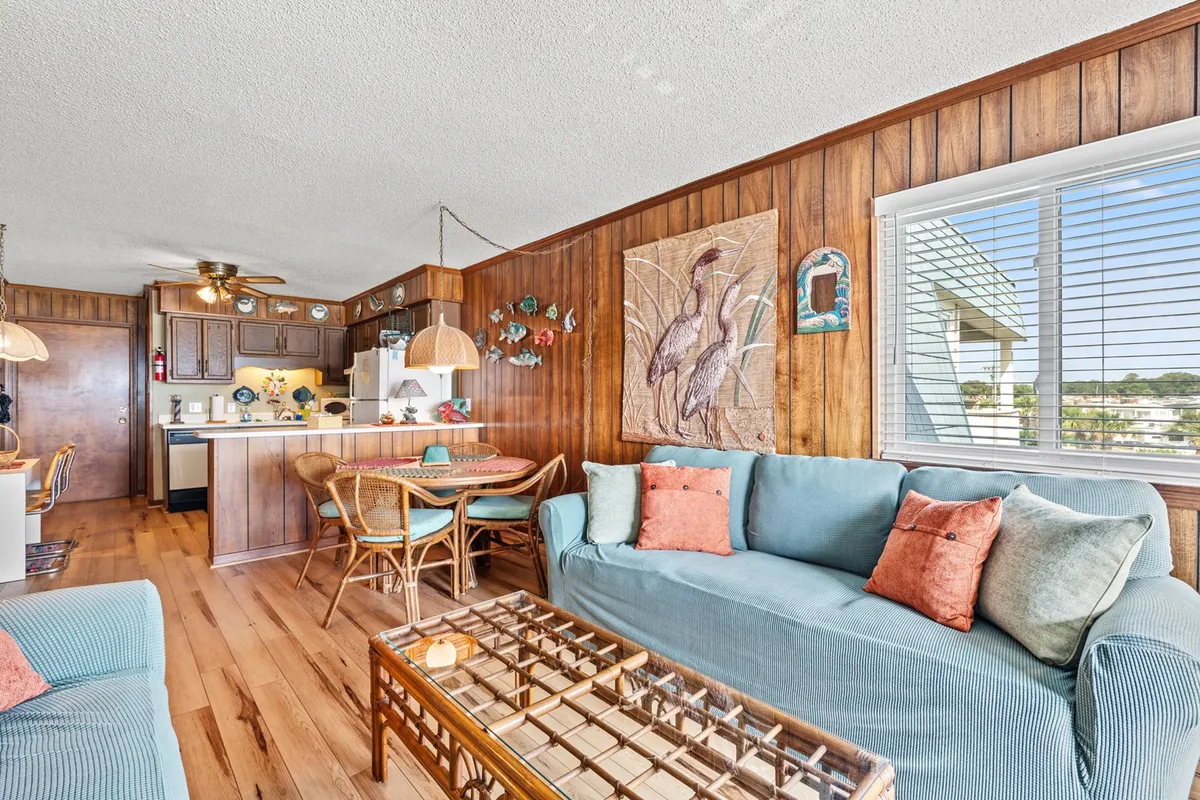 A cozy interior scene featuring comfortable seating, wood-paneled walls, colorful artwork, and a dining area with chairs. The space feels both welcoming and practical for family meals, game nights, or socializing.