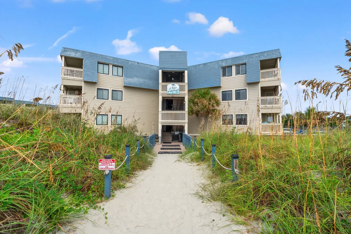 The exterior of the building with a prominent entrance, surrounding greenery, and a pathway leading directly to the beach. The scene emphasizes easy beach access and a tranquil environment.