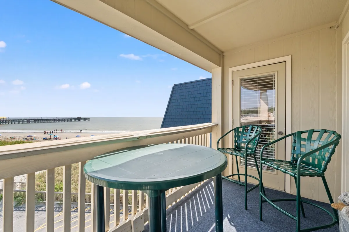A tranquil private balcony furnished with a table and chairs, overlooking the ocean and a pier in the distance. The setting is perfect for sipping morning coffee, reading, or unwinding with evening drinks while taking in the view.