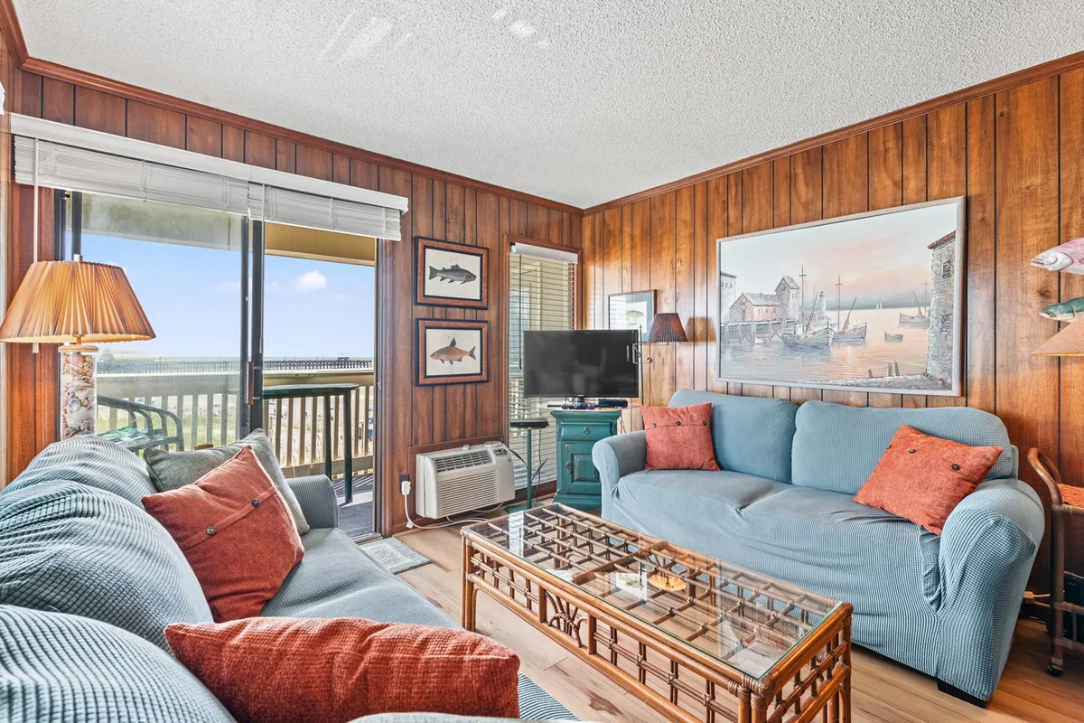A spacious living area with a large sofa, coffee table, tasteful wall art, and a television, with a window allowing in natural light and offering a glimpse of the outdoors. The room exudes comfort and relaxation, perfect for family gatherings or unwinding after a day of adventure.