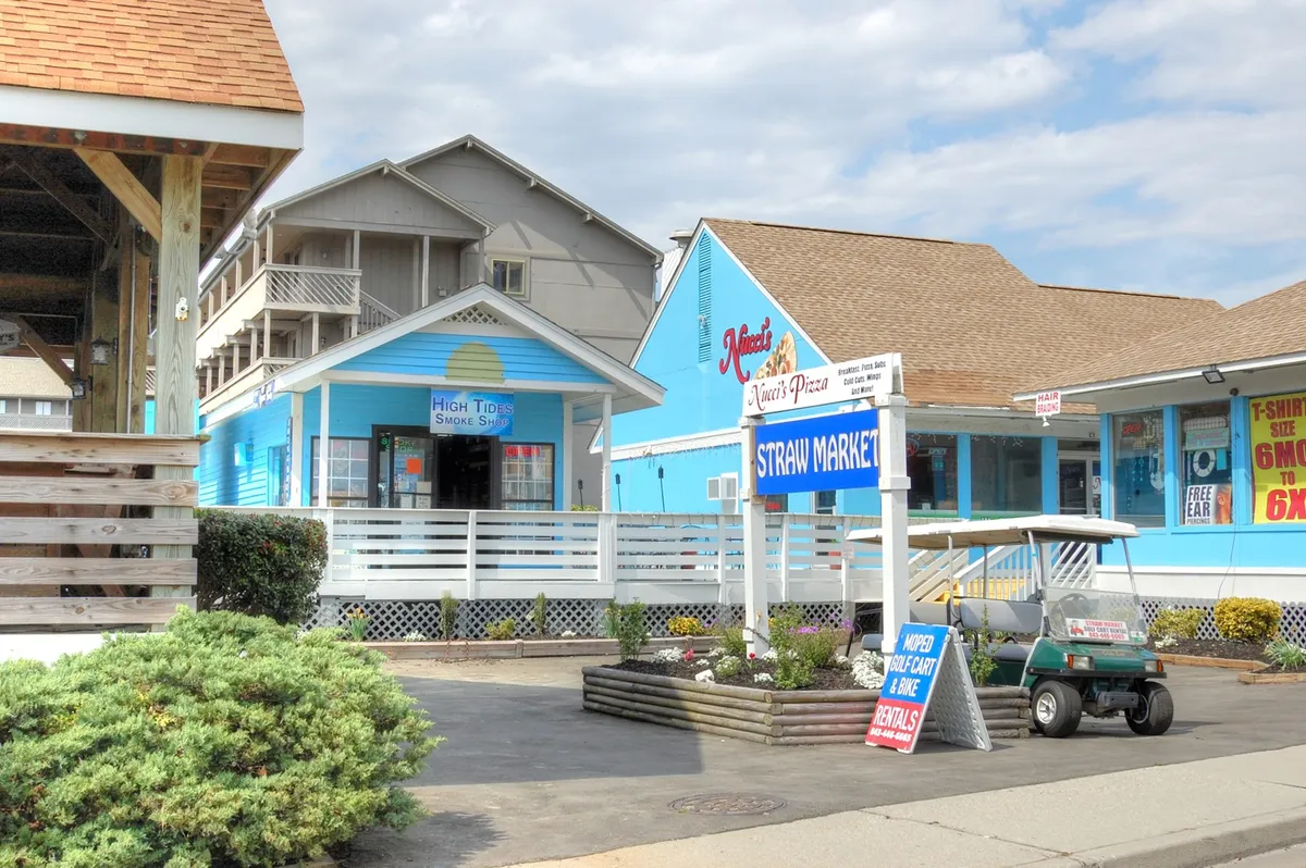 An exterior view of colorful storefronts and signage, with a golf cart in the foreground, creates a lively, welcoming streetscape. This scene references nearby shopping and casual dining, integral to the convenience and variety described for long-term guests.